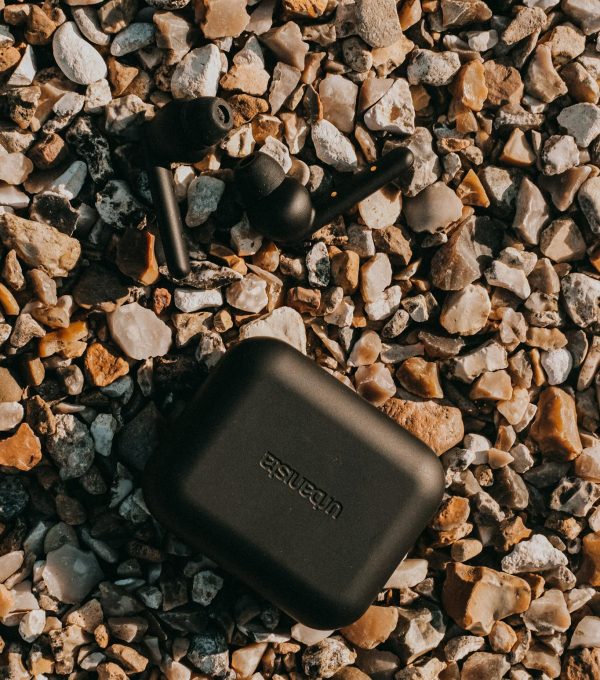 From above of black true wireless earbuds and battery case on dry rocky surface